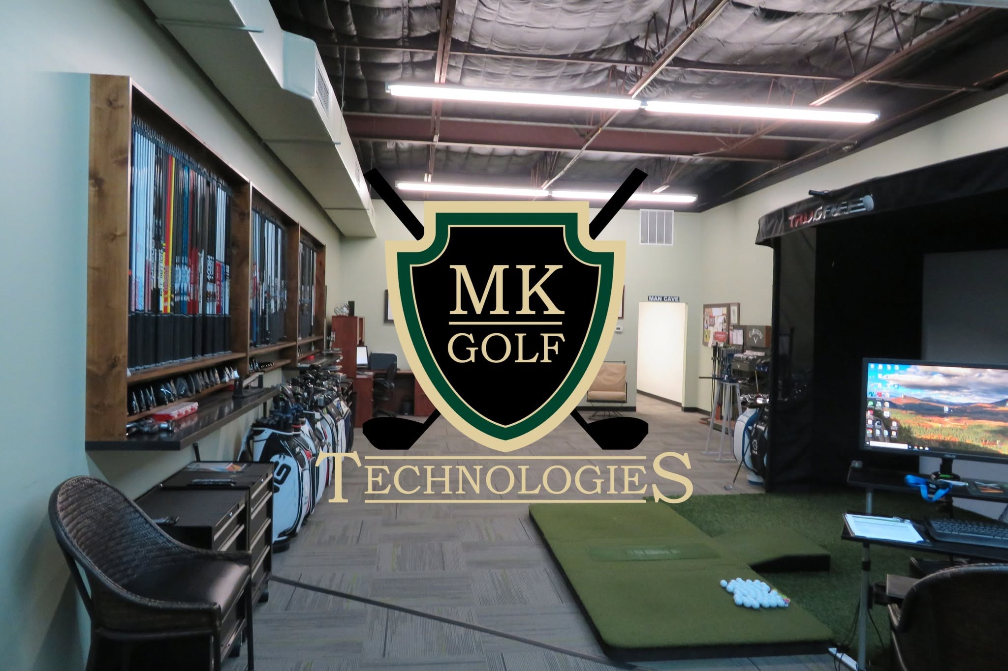 Indoor golf showroom with green practice mats, wall of clubs on the left, and a large MK Golf Technologies crest centered in the foreground.